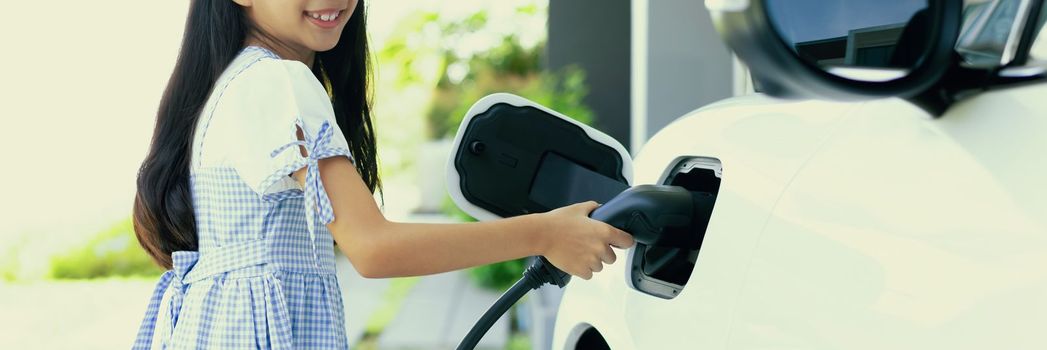 A playful girl holding an EV plug, a home charging station providing a sustainable power source for electric vehicles. Alternative energy for progressive lifestyle.