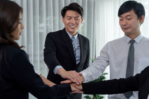Closeup business team of suit-clad businessmen and women join hand stack together and form circle. Colleague collaborate and work together to promote harmony and teamwork concept in office workplace.