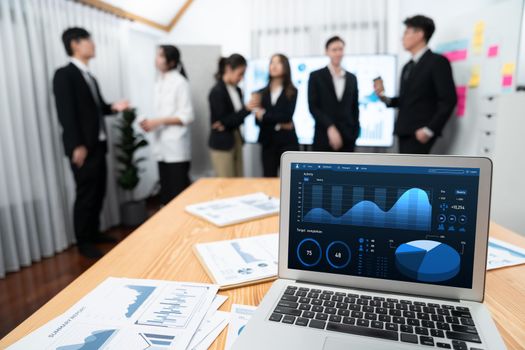 Focus laptop monitor display dashboard report by business intelligence, analyzed financial data for planning market strategy with blur background of standing office worker discussing in harmony office