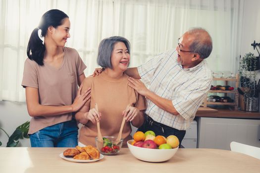Contented family, daughter, father, mother prepare bread veggies and fruit salad together in their kitchen.