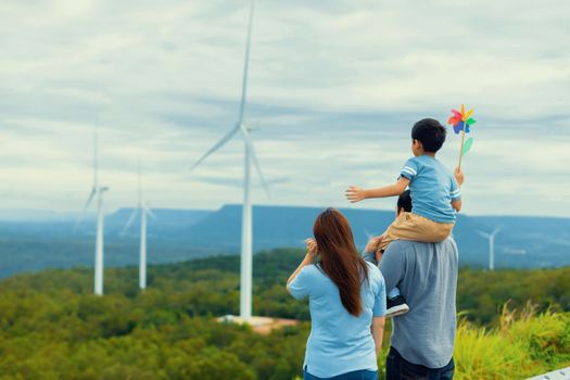 Progressive happy family enjoying their time at wind farm for green energy production concept. Wind turbine generators provide clean renewable energy for eco-friendly purposes.
