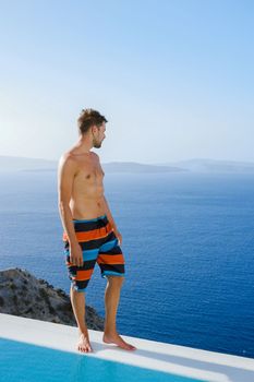 man relaxing in infinity swimming during vacation at Santorini, swimming pool looking out over the Caldera ocean of Santorini, Oia Greece, Greek Island Aegean Cyclades luxury vacation.