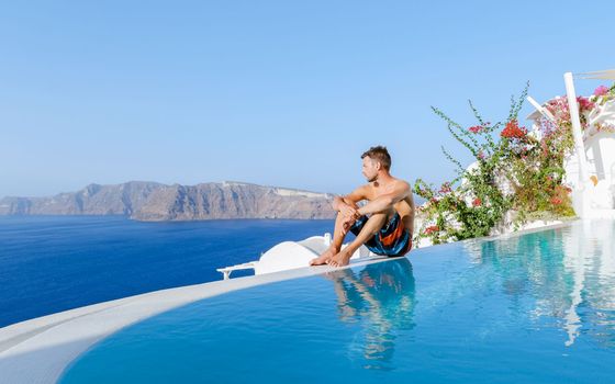 men relaxing in an infinity swimming pool during vacation at Santorini, swimming pool looking out over the Caldera ocean of Santorini, Oia Greece, Greek Island Aegean Cyclades luxury vacation.