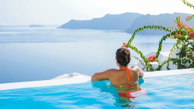 Young Asian women on vacation at Santorini swimming pool looking out over the Caldera ocean of Santorini, Oia Greece, Greek Island Aegean Cyclades.