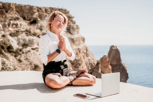Happy girl doing yoga with laptop working at the beach. beautiful and calm business woman sitting with a laptop in a summer cafe in the lotus position meditating and relaxing. freelance girl remote work beach paradise