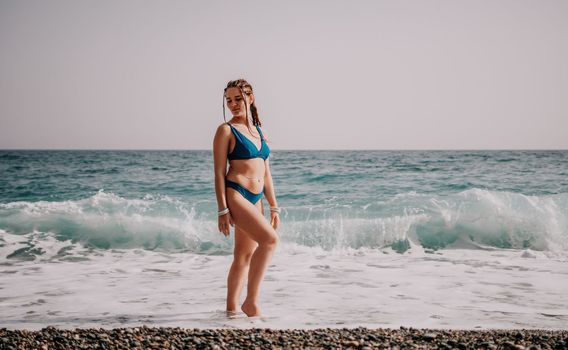 Beach vacation. Hot beautiful woman in sunhat and bikini standing with her arms raised to her head enjoying looking view of beach ocean on hot summer day.