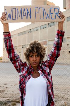 Confident African american demonstration protester looking at camera holding a woman power sign above her head. Feminism and equality concept.