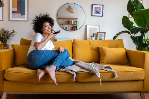 Happy African American woman with curly hair sending voice note message using mobile phone at home sitting on couch. Copy space.Lifestyle concept.