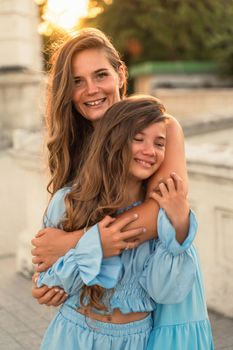 Mother aughter sunset. in blue dresses with flowing long hair against the backdrop of sunset. The woman hugs and presses the girl to her