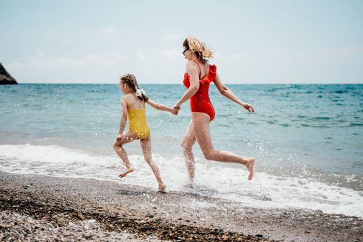 Happy loving family mother and daughter having fun together on the beach. Mum playing with her kid in holiday vacation next to the ocean - Family lifestyle and love concept.