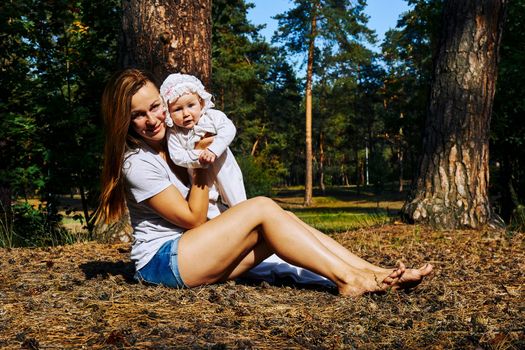 a very young child, especially one newly or recently born. Young pretty mother with a cute breast newborn baby in a sunny forest.