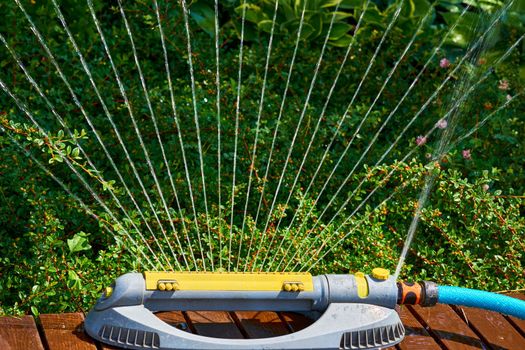 the supply of water to land or crops to help growth, typically by means of channels. Irrigation system, sprinkler watering flowers on a hot day in a city park.
