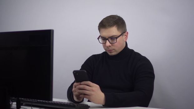 The young IT specialist got tired of working and started chatting on the phone. A man with glasses in the office with a smartphone in his hands. 4k