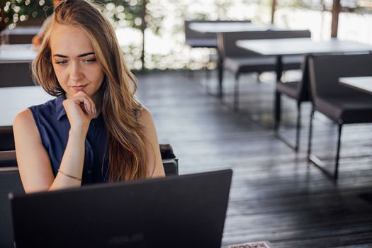 Young business woman working at a computer in a cafe. A young downshifter girl works at a laptop, working day.