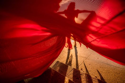 Sunrise red dress. A woman in a long red dress against the backdrop of sunrise, bright golden light of the sun's rays. The concept of femininity, harmony