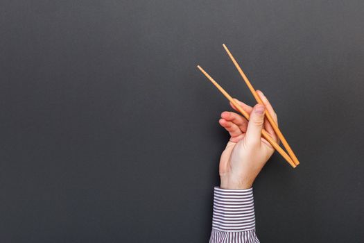 Creative image of wooden chopsticks in male hands on black background. Japanese and chinese food with copy space.