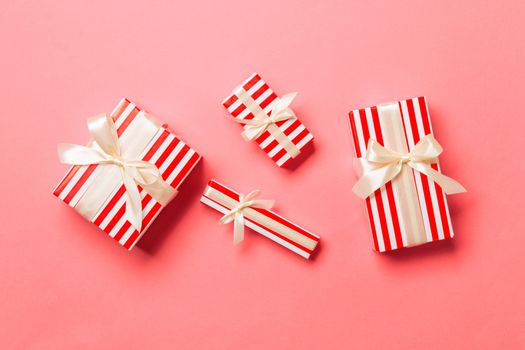 wrapped Christmas or other holiday handmade present in paper with yellow ribbon on living coral background. Present box, decoration of gift on colored table, top view.