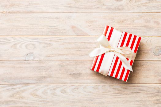 Beautiful gift box with a colored bow on the orange wooden table. Top view with copy space for you design. Christmas concept.