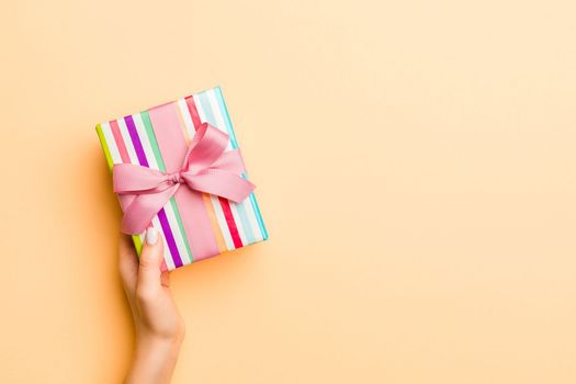 Flat lay of woman hands holding gift wrapped and decorated with bow on gold background with copy space. Christmas and holiday concept.