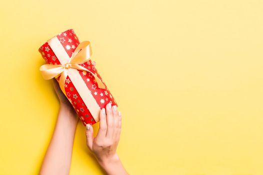 Woman arms holding gift box with colored ribbon on yellow table background, top view and copy space for you design.