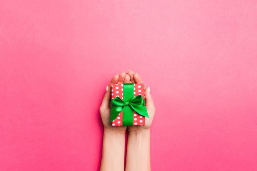 Girl Hands holding craft paper gift box with as a present for Christmas or other holiday on pink background, top view with copy sppace.