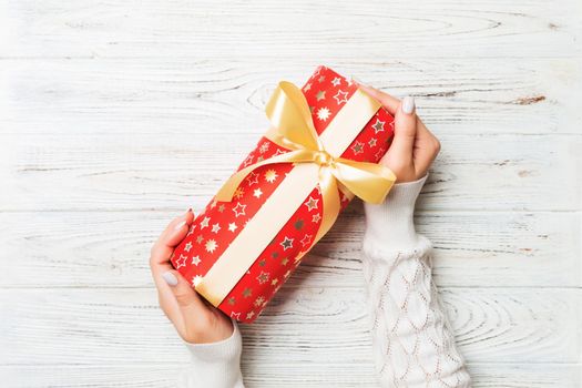 Woman hands give wrapped christmas or other holiday handmade present in colored paper . Present box, decoration of gift on white rustic wooden table, top view with copy space