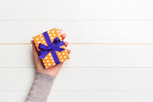 woman hands holding gift wrapped and decorated with colored bow top view on white wooden table Holiday concept with copy space .