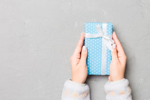 Female hands holding present on grey cement background. Festive backdrop for Christmas holidays or other holiday . Flat lay style top view with copy space.