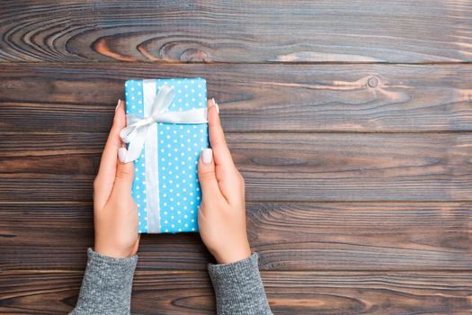 woman hands holding gift wrapped and decorated with colored bow top view on Dark wooden table Holiday concept with copy space .