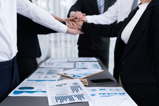 Focus financial report with statistic charts analyzed by BI papers on meeting table at conference room with blur business colleague people put hand stack together in background as harmony concept.