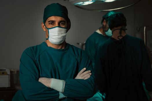 Portrait of surgical team leader in sterile operating room with his team and patient undergoing surgery. Confident and professional surgeon in full protective wear provide medical care to his patient.