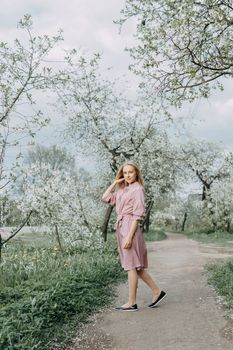 Blonde girl on a spring walk in the garden with cherry blossoms. Female portrait, close-up. A girl in a pink polka dot dress