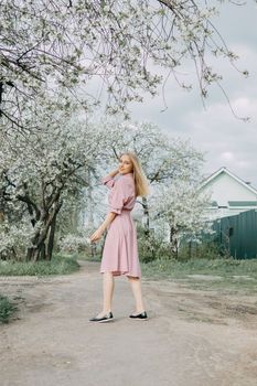 Blonde girl on a spring walk in the garden with cherry blossoms. Female portrait, close-up. A girl in a pink polka dot dress