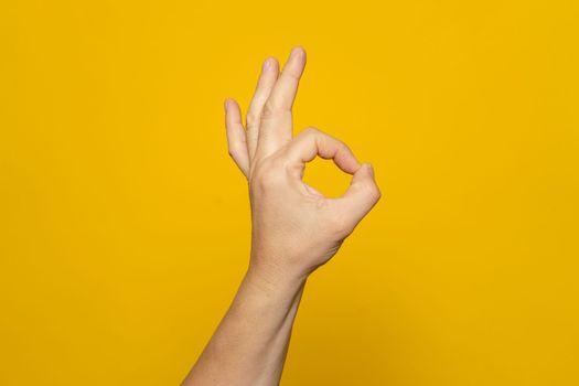 Strong hand of man making the ok gesture isolated on yellow background