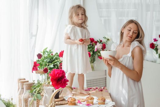 A little blonde girl with her mom on a kitchen countertop decorated with peonies. The concept of the relationship between mother and daughter. Spring atmosphere