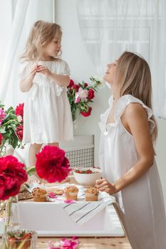 A little blonde girl with her mom on a kitchen countertop decorated with peonies. The concept of the relationship between mother and daughter. Spring atmosphere