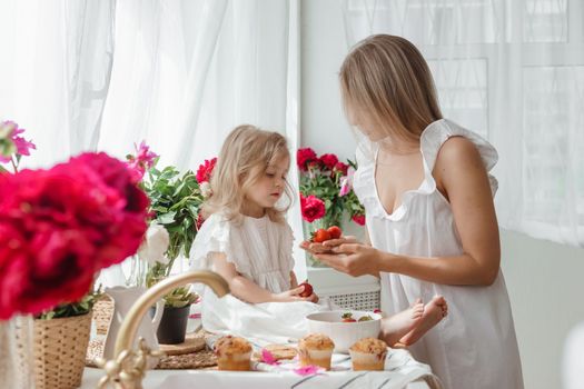 A little blonde girl with her mom on a kitchen countertop decorated with peonies. The concept of the relationship between mother and daughter. Spring atmosphere