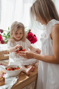 A little blonde girl with her mom on a kitchen countertop decorated with peonies. The concept of the relationship between mother and daughter. Spring atmosphere