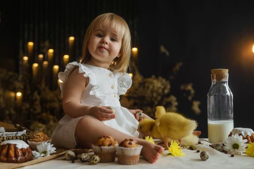 A little girl is sitting on the Easter table and playing with cute fluffy ducklings. The concept of celebrating happy Easter