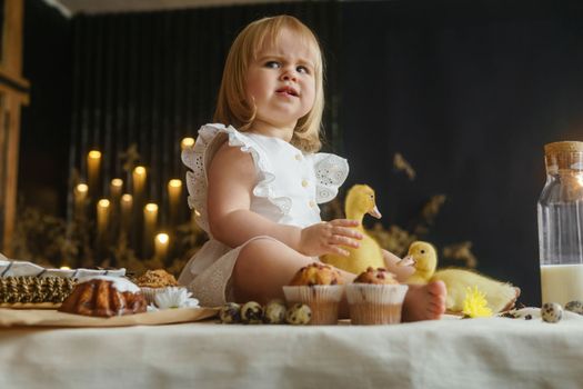 A little girl is sitting on the Easter table and playing with cute fluffy ducklings. The concept of celebrating happy Easter