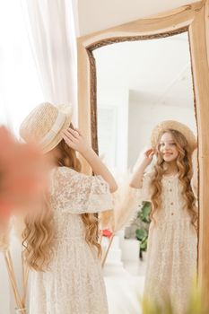 A beautiful teenage girl with long hair measures a straw hat in front of a mirror. Self-admiration of a blonde. selective focus