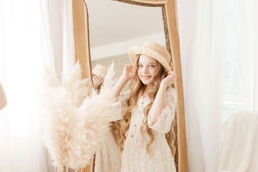 A beautiful teenage girl with long hair measures a straw hat in front of a mirror. Self-admiration of a blonde. selective focus