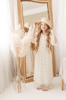 A beautiful teenage girl with long hair measures a straw hat in front of a mirror. Self-admiration of a blonde. selective focus