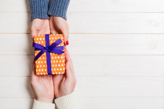 Top view of a gift in male and female hands on wooden background. Congratulation of each other concept. Copy space.