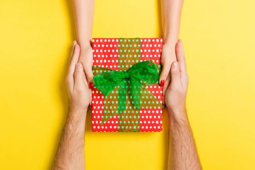 Top view of two people sharing a present on colorful background. Holiday and surprise concept. Copy space.