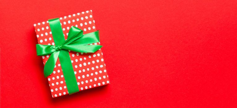 Top view Christmas present box with green bow on red background with copy space.