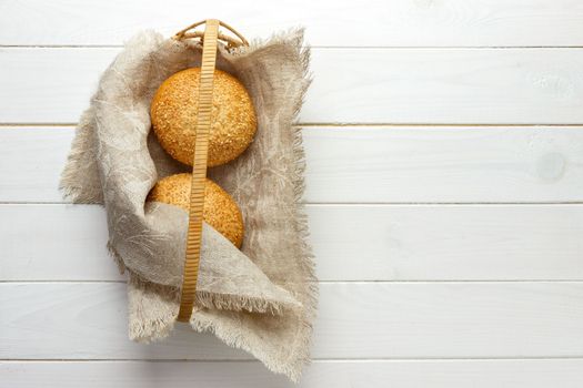 baked bun with sesame seedsin basket lying on fabric.