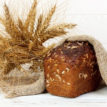 Bread with seeds and wheat ears on wooden table.