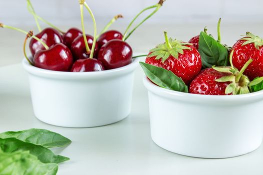 Ripe strawberries, mint and black cherry in bowls.