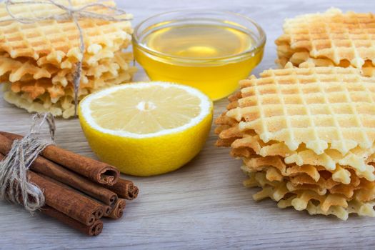 Waffle with honey,cinnamon, lemon on a light wooden background.